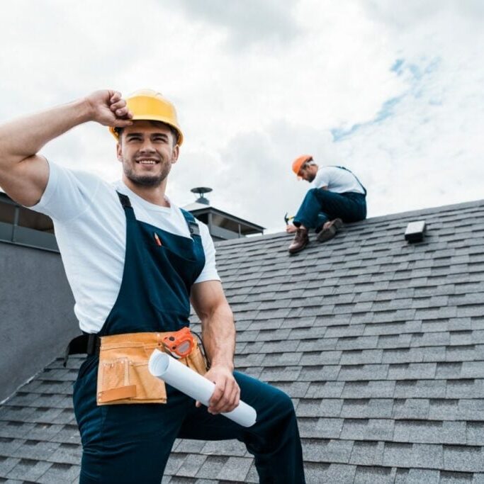 selective-focus-of-happy-repairman-holding-rolled-paper-while-coworker-repairing-roof-e1625561369341 selective-focus-of-happy-repairman-holding-rolled-paper-while-coworker-repairing-roof-e1625561369341